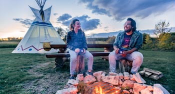 2 friends talking by a fire, infront of a tipi